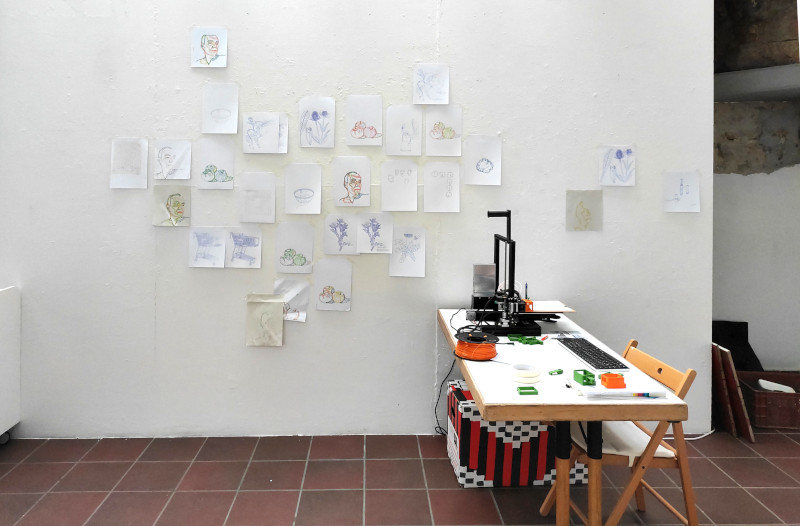 Illustration of the exhibition situation in the BBK studio for Druckkunmst 2023: Table with 3D printer, on the wall printouts of the device converted to a 2D printer.
